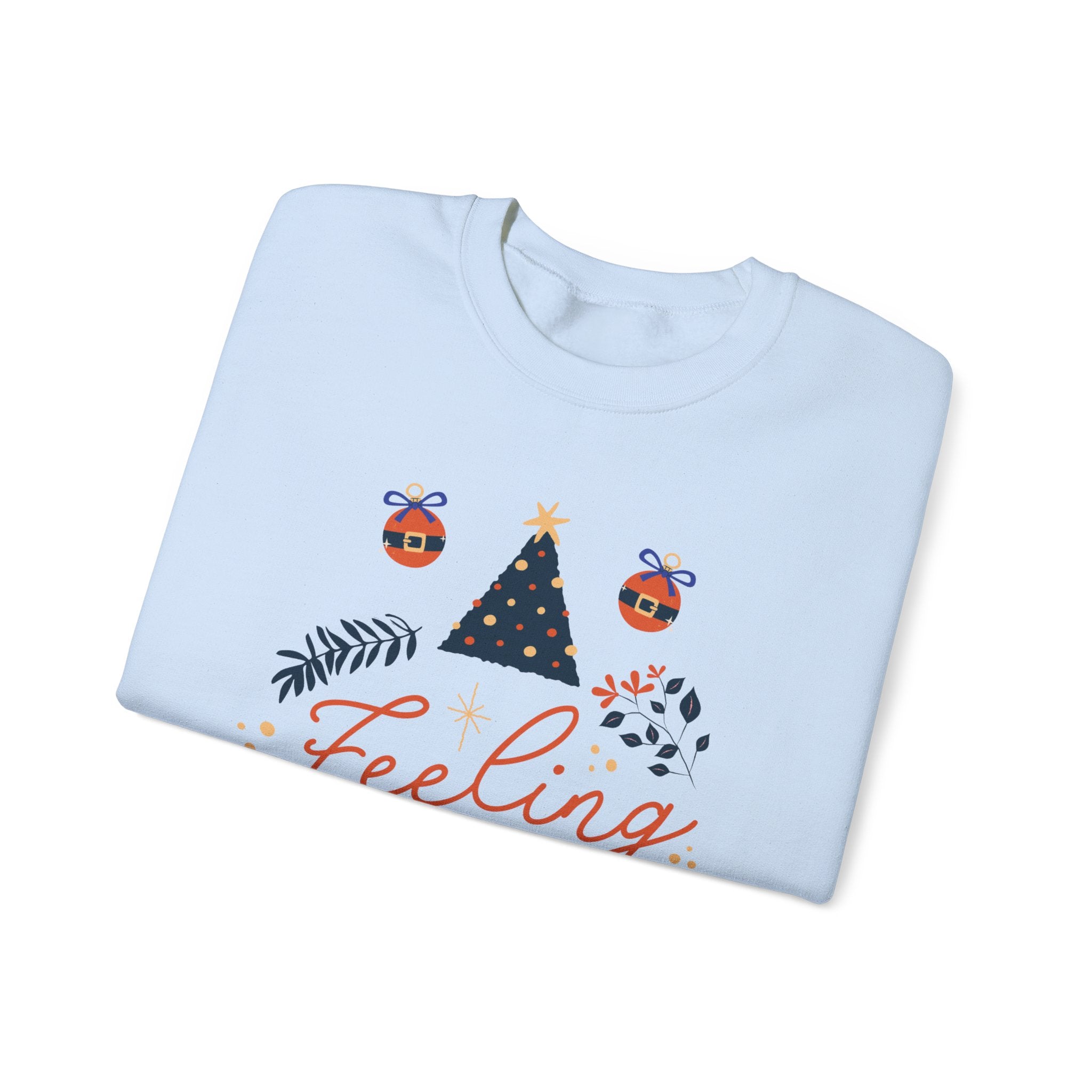Folded white sweatshirt with 'Feeling' text, Christmas tree, and ornament graphics.